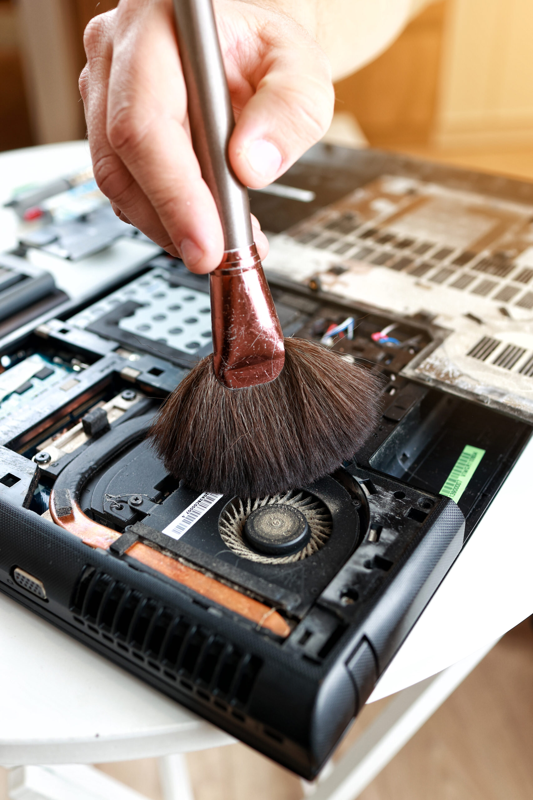 Repaiman with brush is cleaning disassembled laptop parts. Technical support and fixing gadgets problems. Servicing, repairing, cleaning, maintaining computers. Repair shop. Hardware maintenance