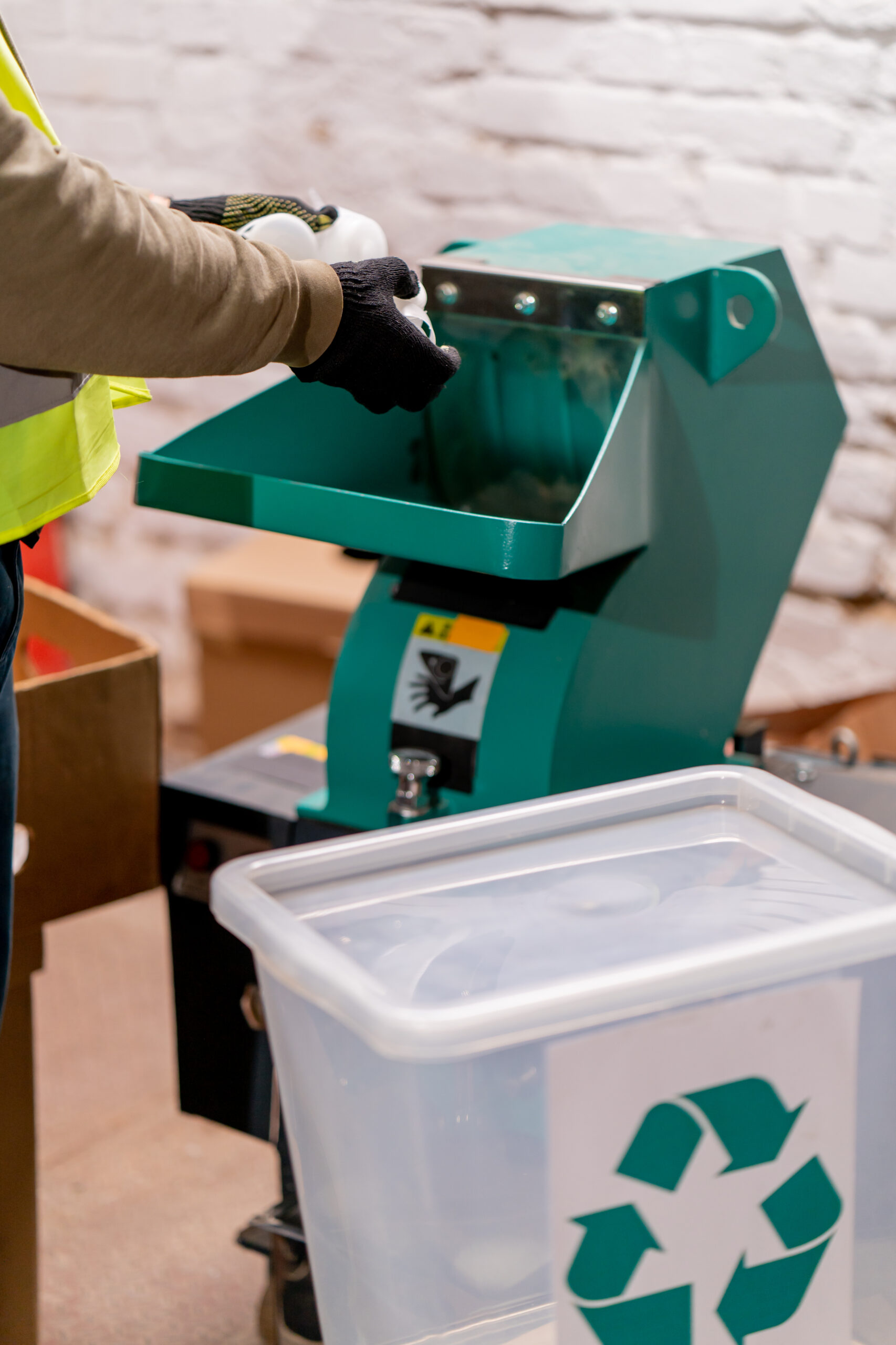 Close-up shot of male hands in gloves pouring plastic caps into a shredding apparatus for recycling